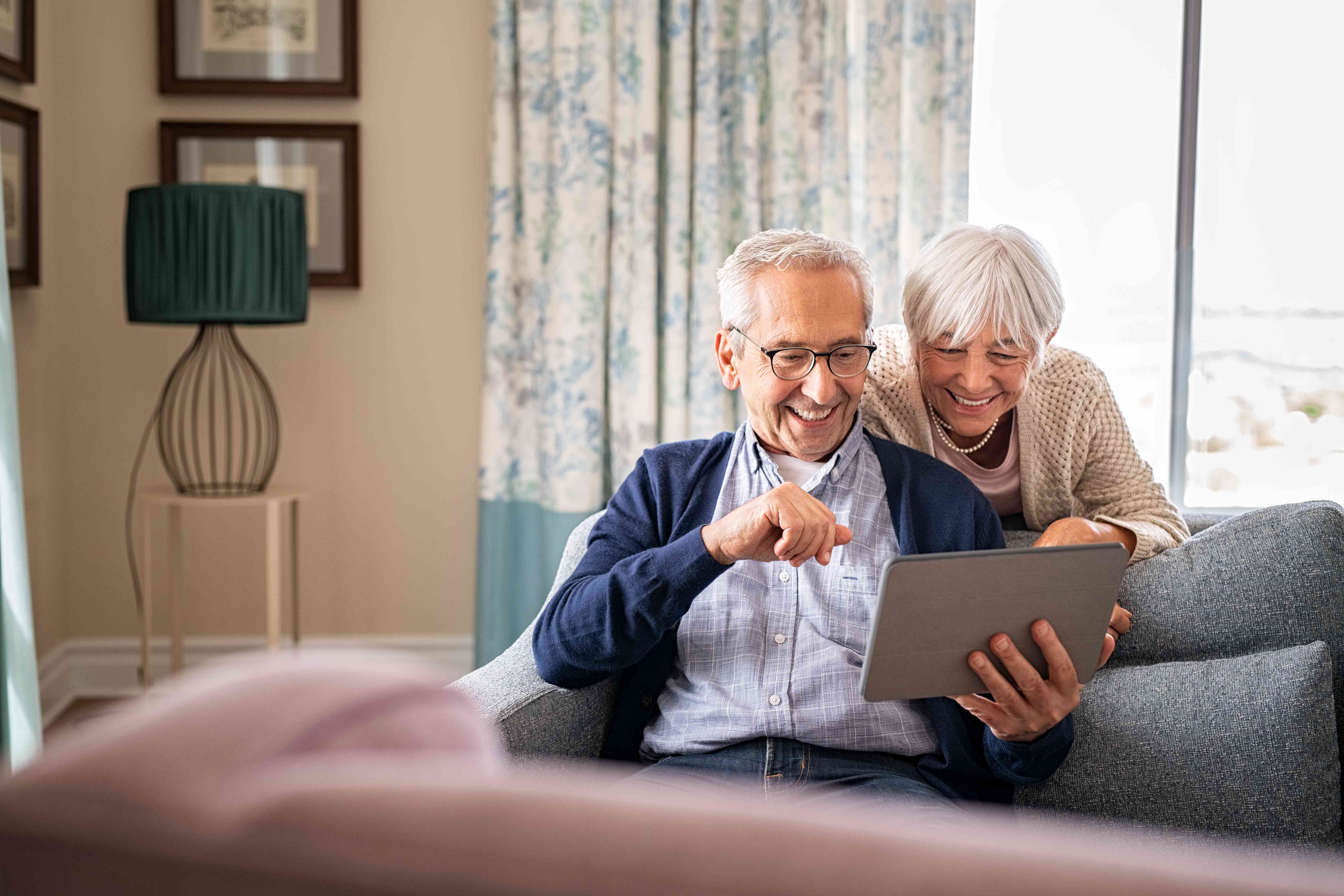 Older couple at home in their living room looking happily at a tablet