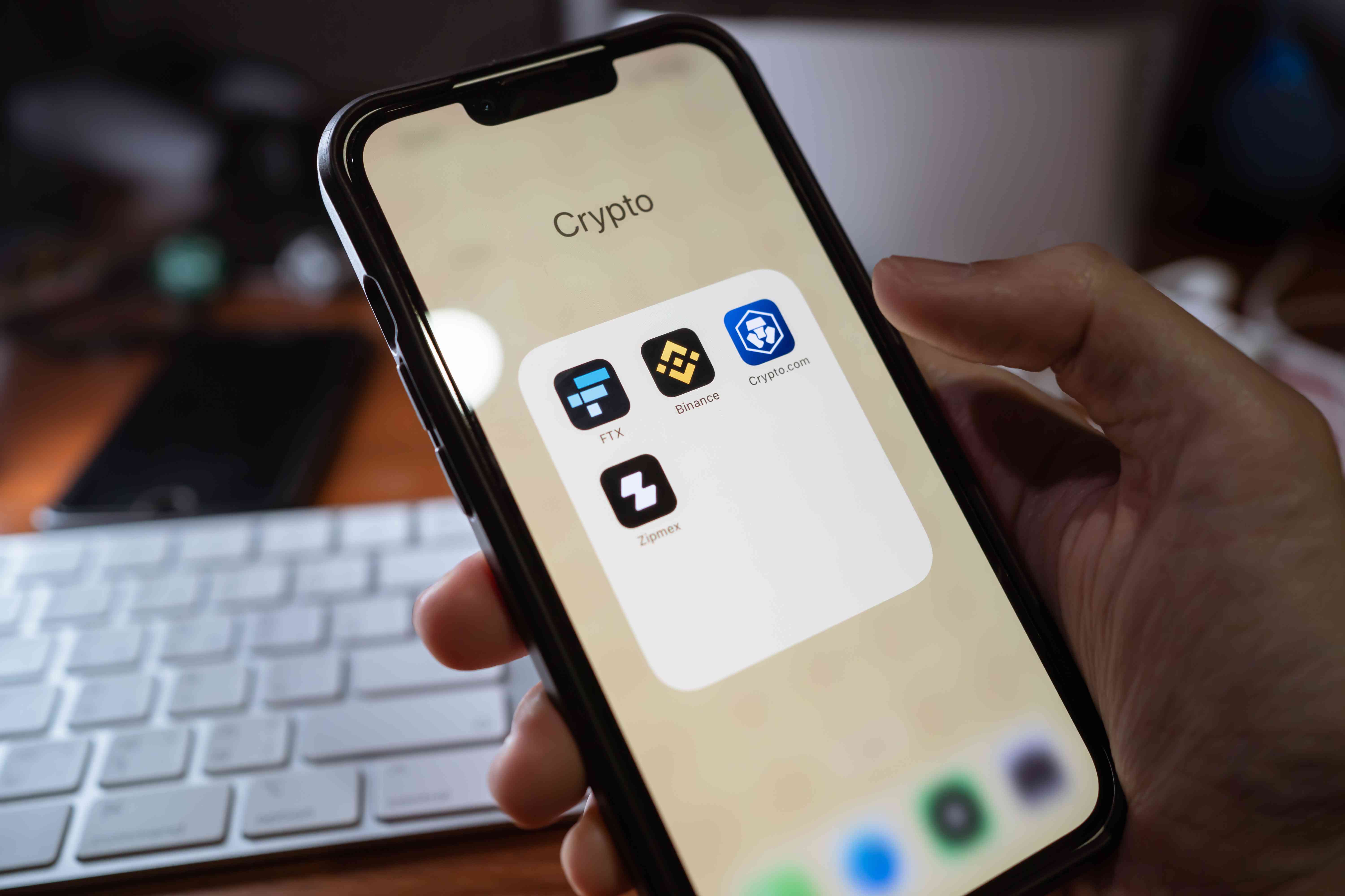 A person holds an iPhone displaying cryptocurrency trading apps.