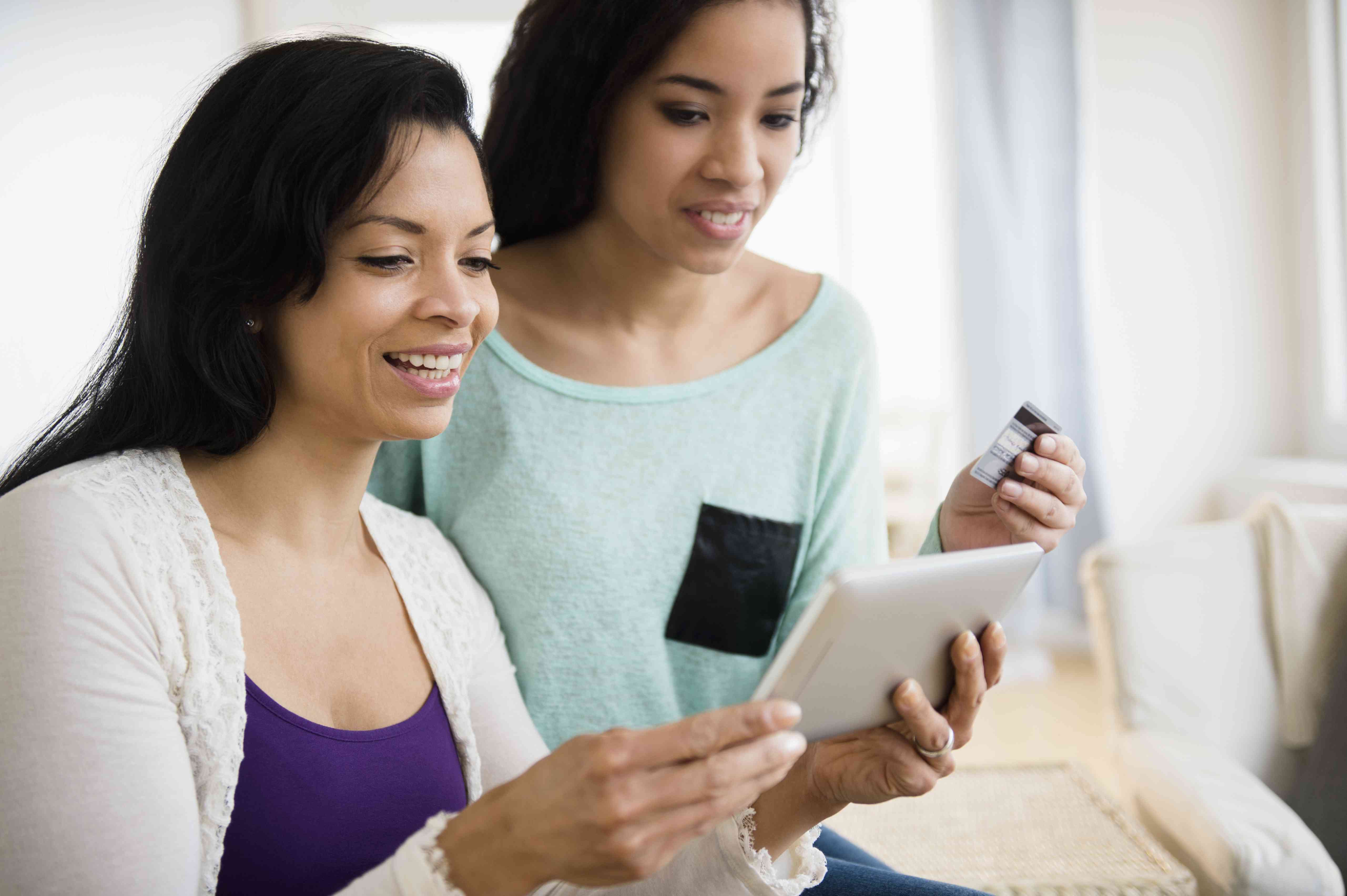 A mother and a daughter look at a tablet while also holding a credit card