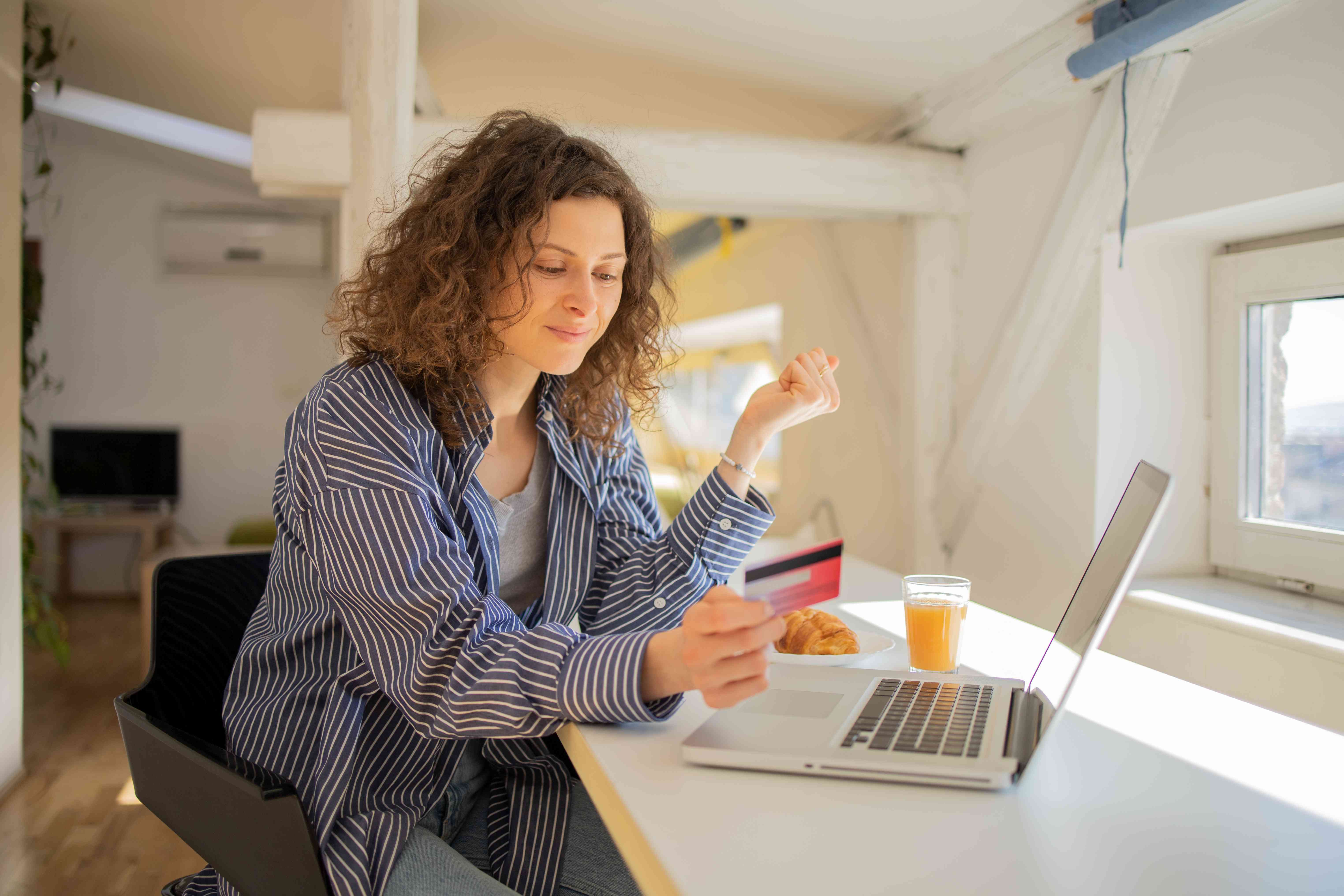 Woman sitting at a desk holding a credit card in front of an open laptop