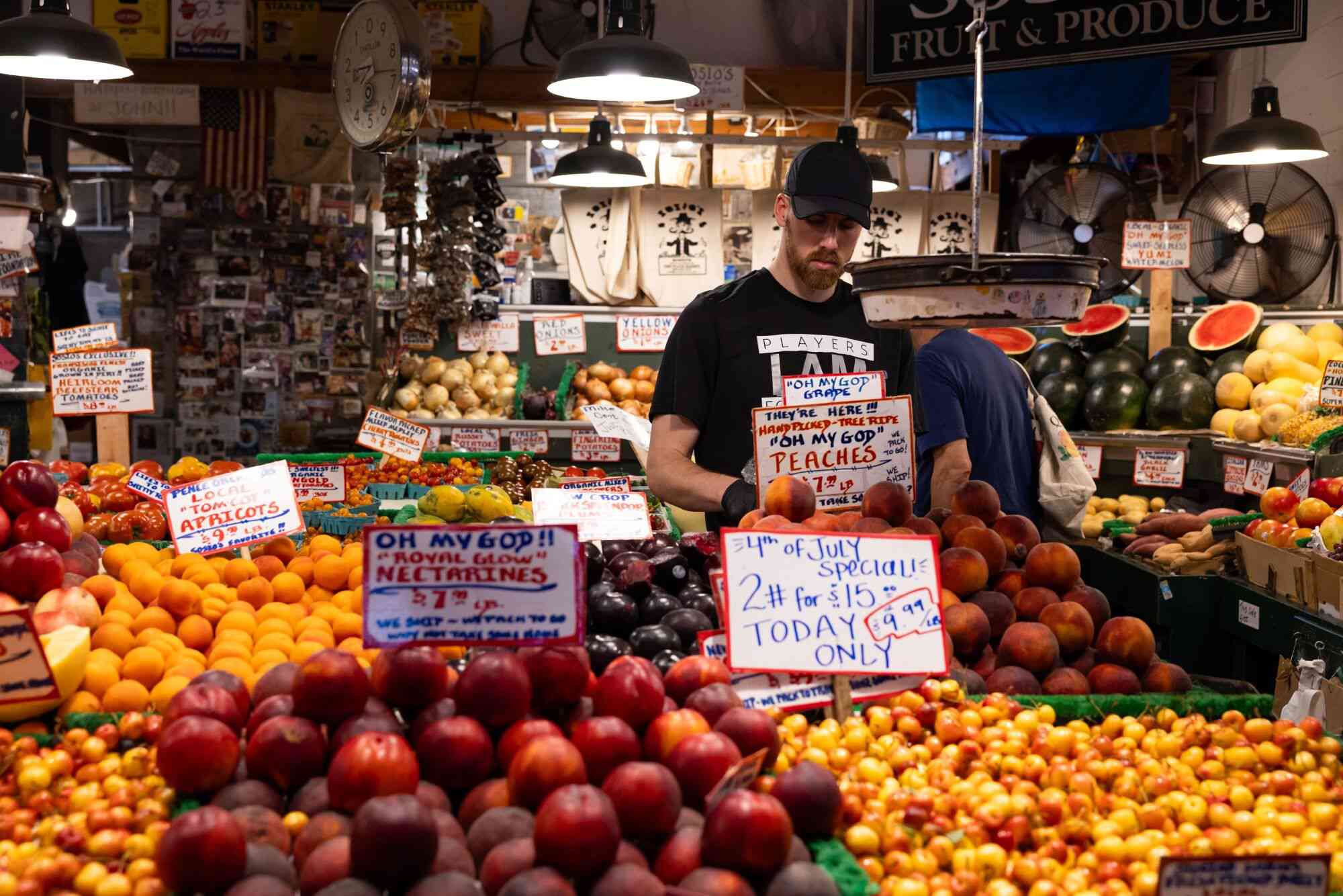  worker arranges peaches at a fruit stand in the Pike Place Market in Seattle, Washington, US, on Thursday, July 4, 2024.